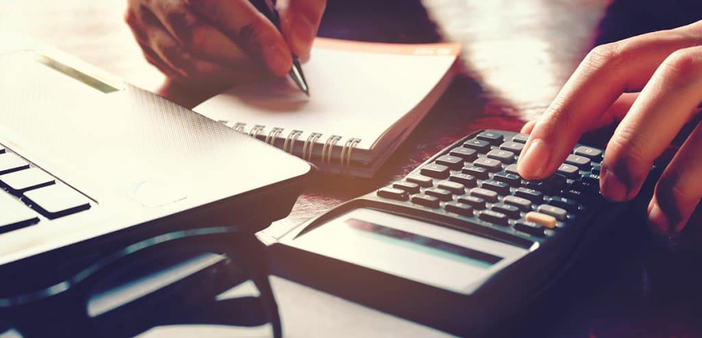 Close up woman hand using calculator and writing make note with calculate about cost at home office.